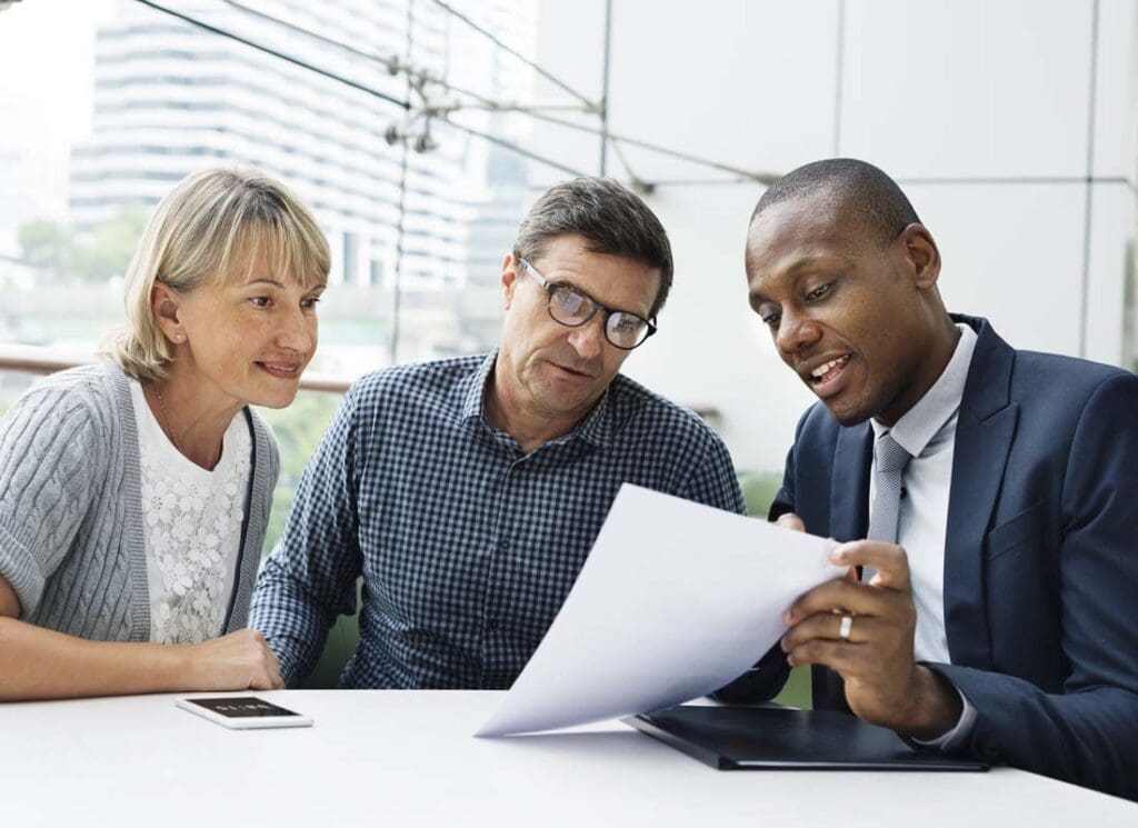 Insurance Companies - An Agent in a Suit Explains Options to Clients, a Mature Couple, in an Office Filled with Large Windows